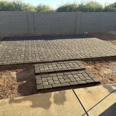 Charcoal paver patio being laid against a block wall in an Arizona City backyard