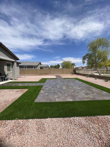 Wide view of the completed backyard with paver patio, turf, and decorative rock