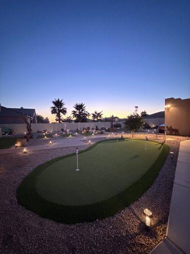 The putting green lit at dusk with the sunset behind the palms