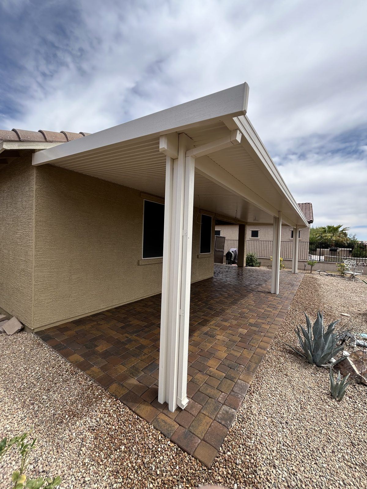Warm-blend paver patio under a covered white patio roof, edged in decorative rock