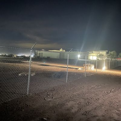 Commercial chain link fence line installed and repaired on a dirt lot in Eloy, photographed at night