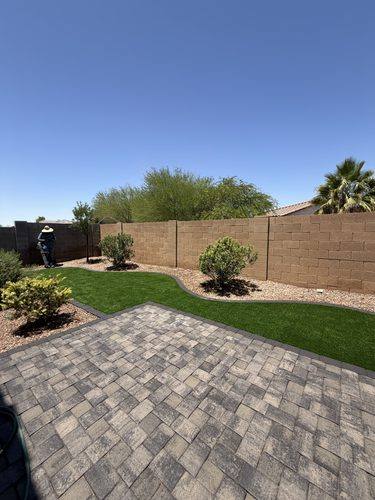 Paver patio in the foreground with turf and new trees along the back wall