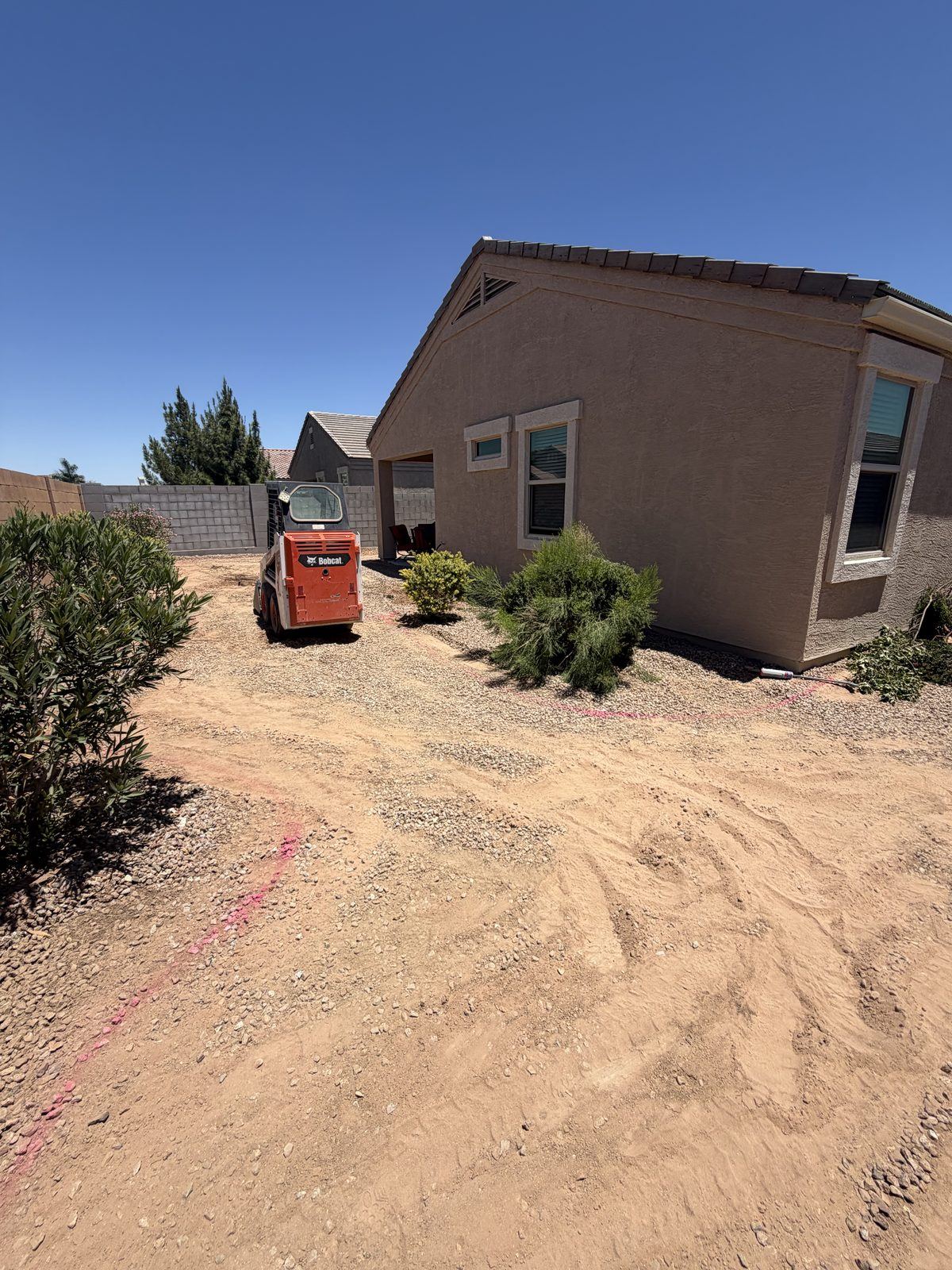 Skid steer grading a Casa Grande side yard down to dirt, with the new layout marked in paint