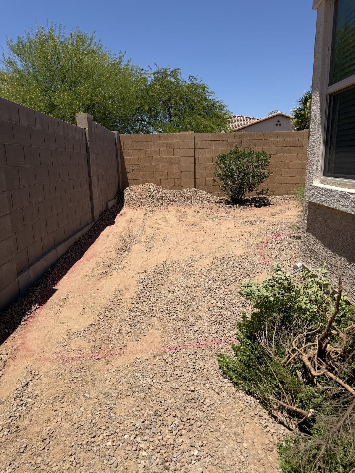 Side yard graded flat to dirt with gravel piled along the block wall, layout lines painted on the ground