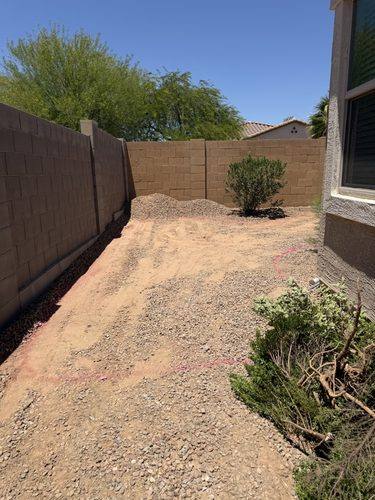 Side yard graded to dirt with gravel piled along the back wall before landscaping
