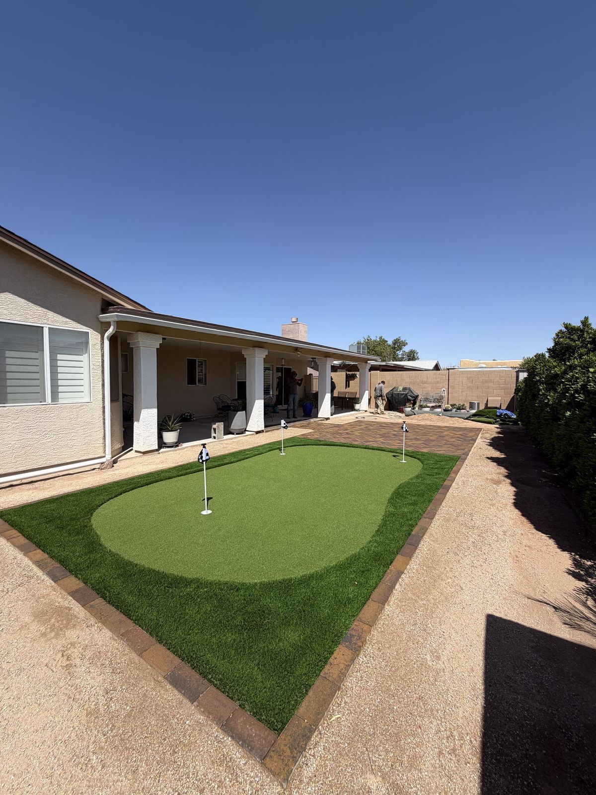 Backyard putting green built from artificial turf next to a paver patio