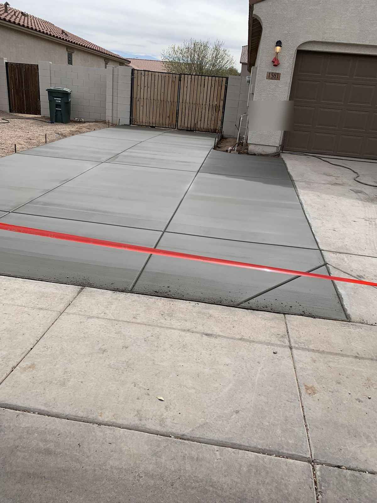 Freshly poured and finished concrete slab extension beside an existing driveway, taped off to cure