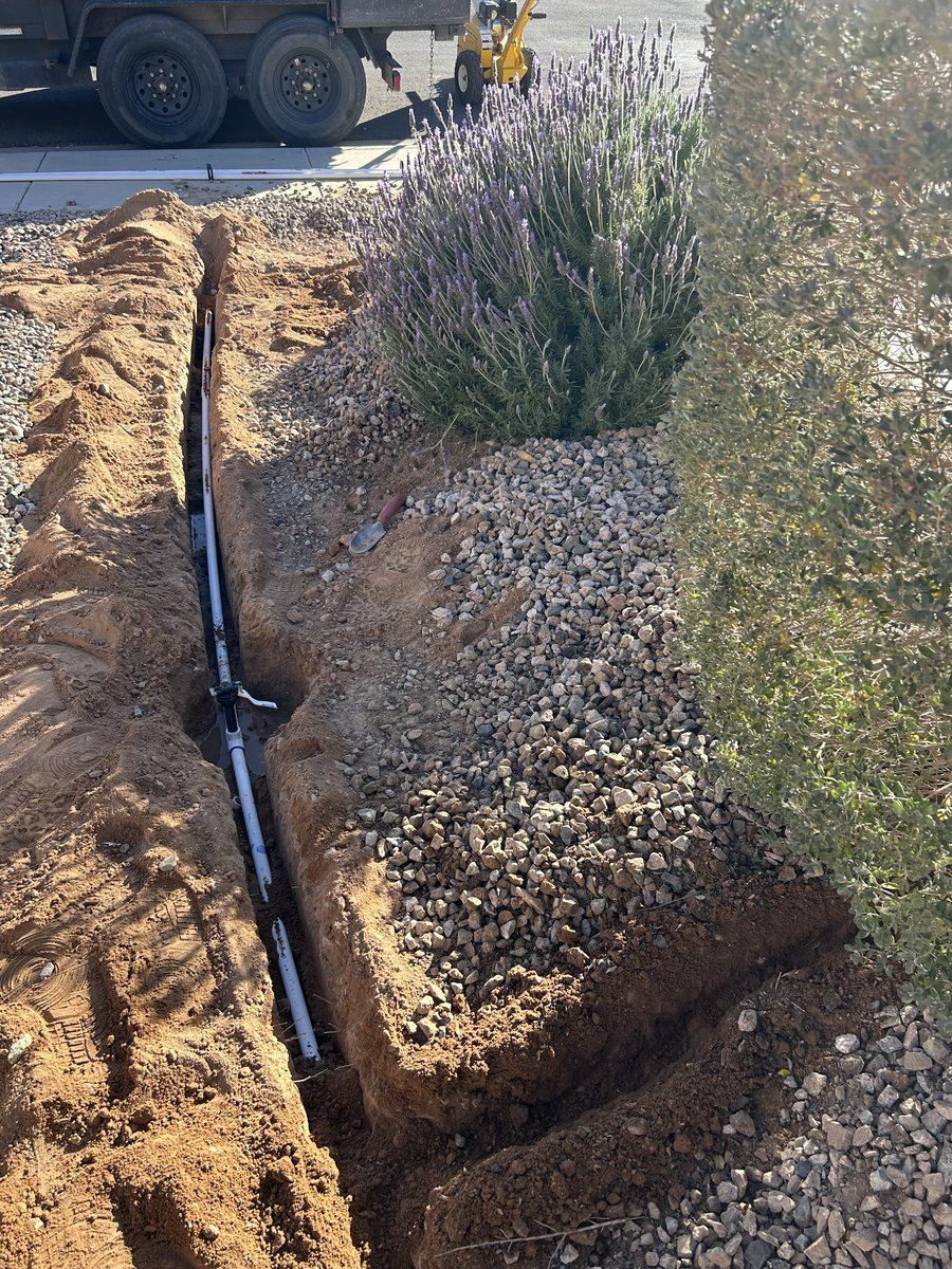 Open trench with new PVC irrigation mainline run beside a planting bed