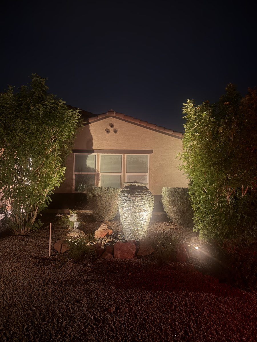Stacked stone urn water feature lit from below at night by low-voltage landscape lighting