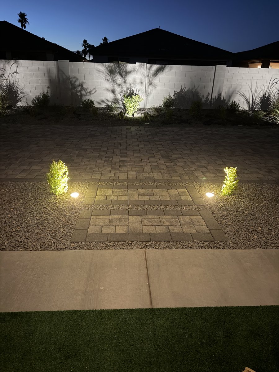 Low-voltage path lights and shrub uplighting along a paver walkway after dark