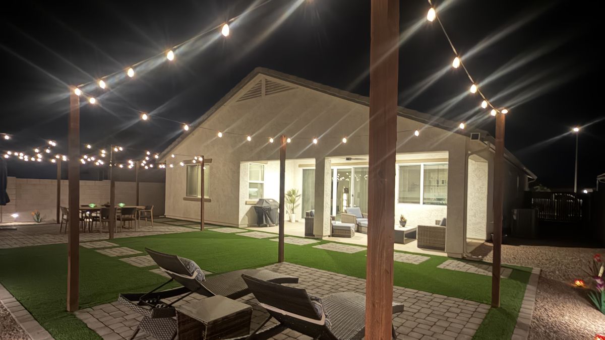 The same backyard at night, built to the render — string lights over the paver lounge pad and turf