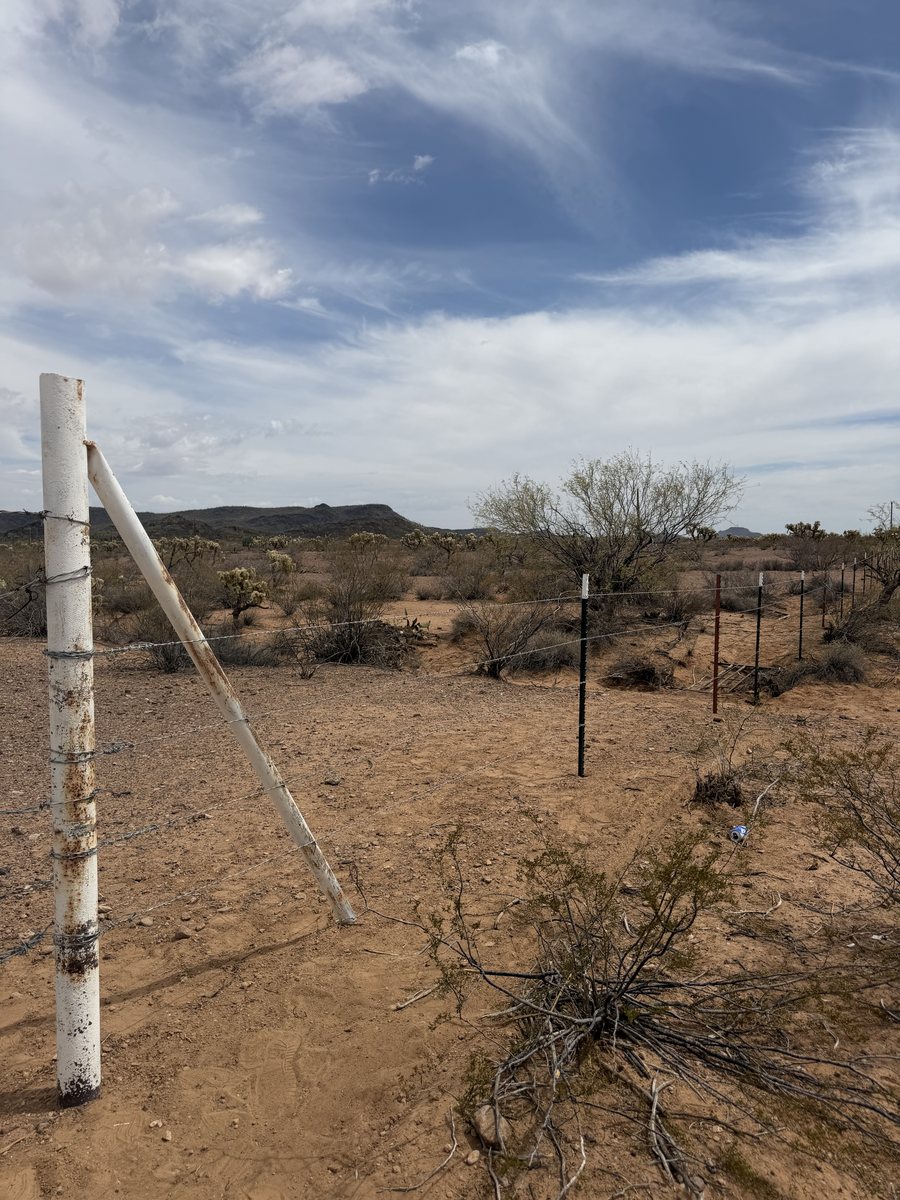 Wire property fence with braced corner post running across open desert acreage